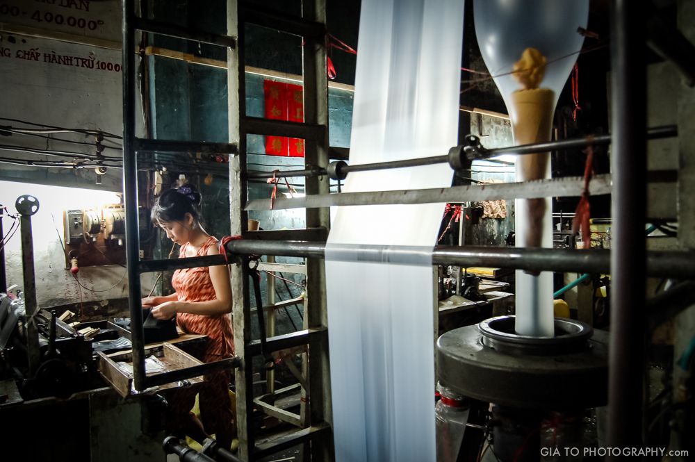 Woman working in a plastic bag factory. This small factory in Viet-Nam uses 30 years old rusty machinery, and still functioning. She's not dressed as a worker, because this is a family business. Her person represents one reality of developing country, not a cliche built for western eyes and expectations.